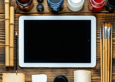 A modern iPad Pro with a calligraphy brush app open alongside high-end physical brushes